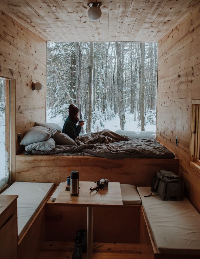 todo-tiny-house-interior-madera-cama-ventana-mujer-bosque-nieve